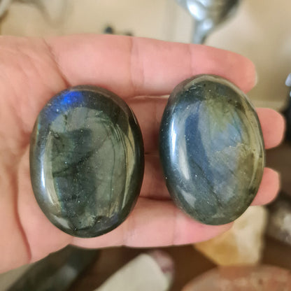 Two polished labradorite stones with a greenish-blue and blue sheen, held in a person's hand.