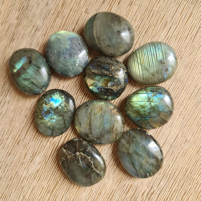 A collection of smooth, round Labradorite pebbles with a polished surface, displaying a natural pattern of colors primarily in dark shades with hints of blue and green iridescence.