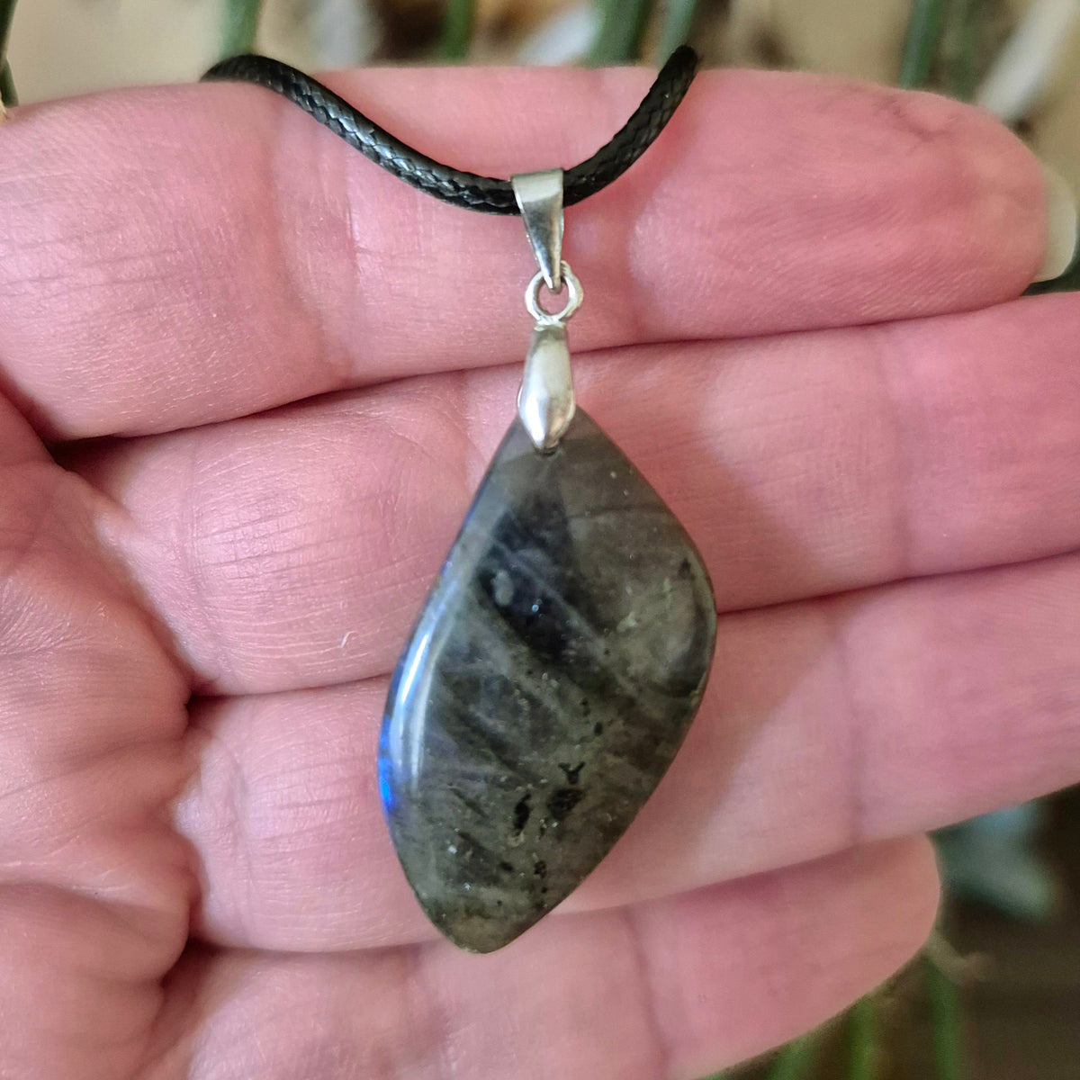A hand holding a labradorite pendant necklace with a silver chain and black leather closure.