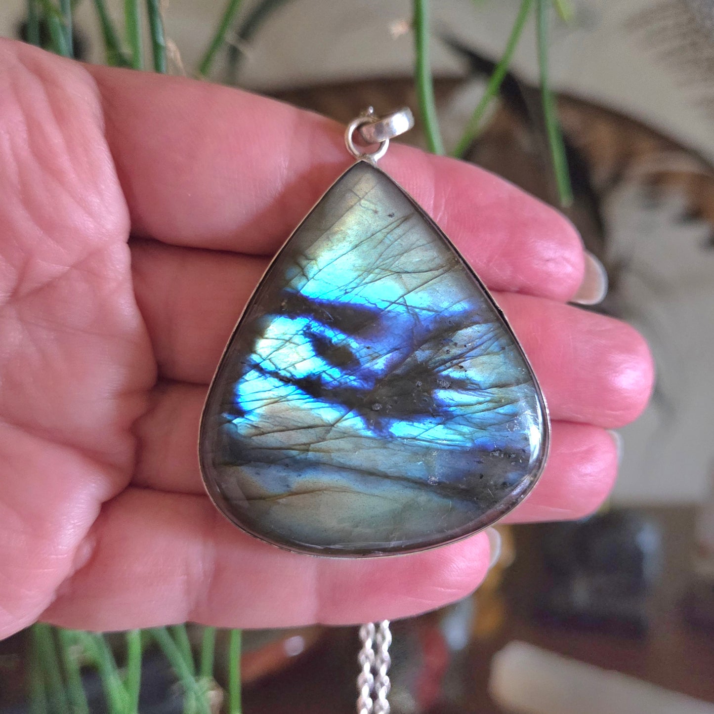 Teardrop-shaped labradorite pendant held in a hand with a blurred background