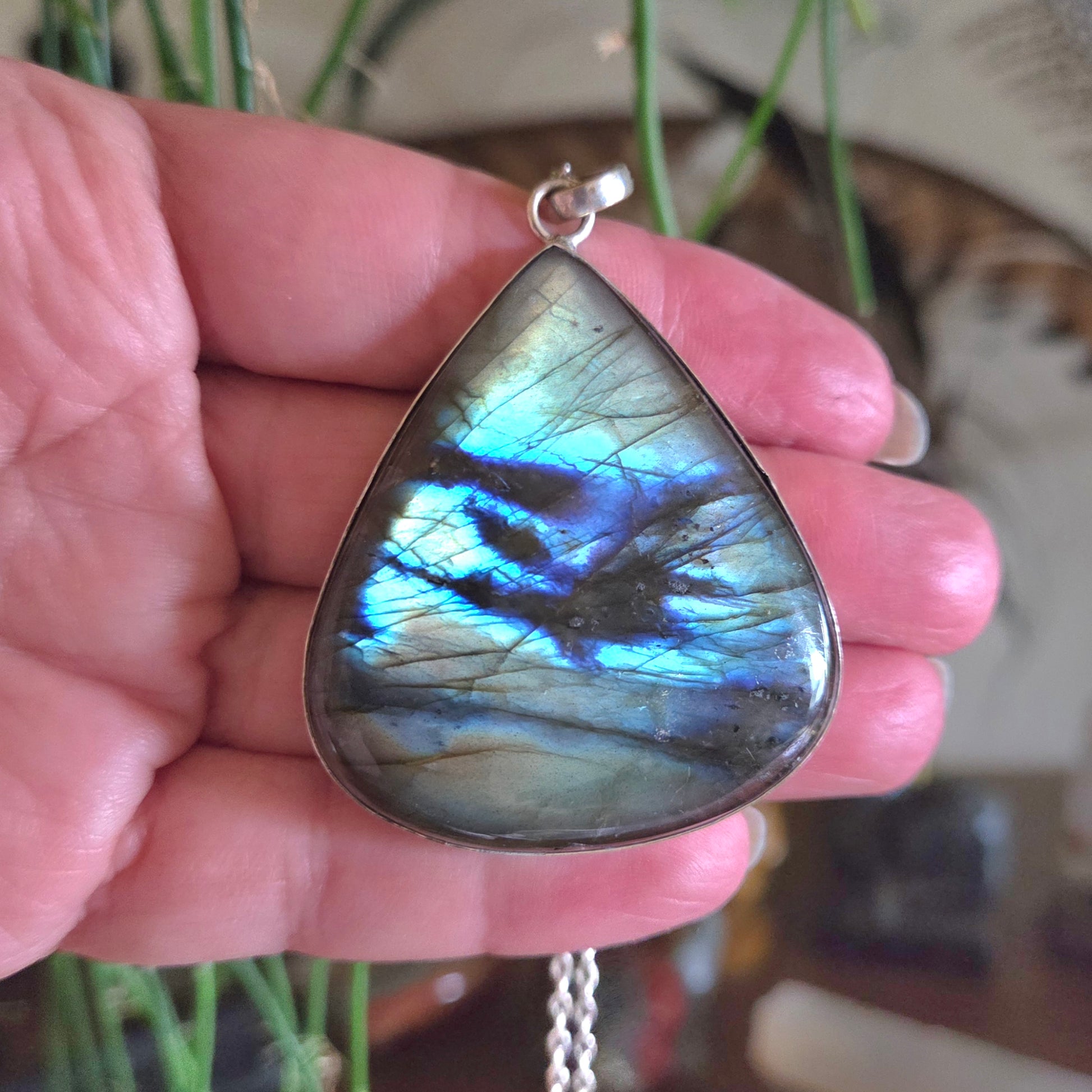 Teardrop-shaped labradorite pendant held in a hand with a blurred background