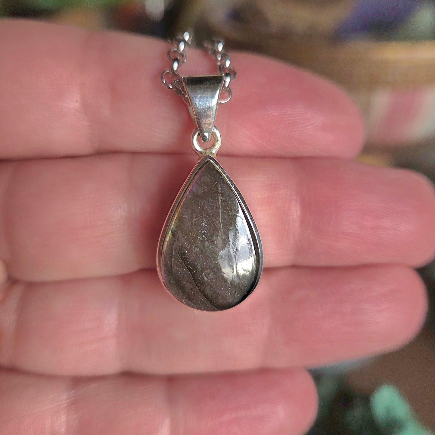 Teardrop-shaped pendant on a chain held in a hand