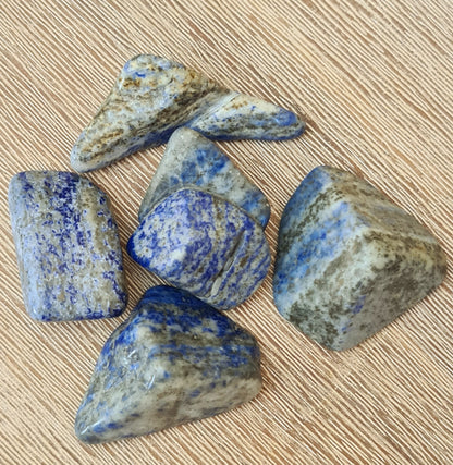 Several polished lapis lazuli chunks with a blue coloring and natural patterns, placed on a beige background.