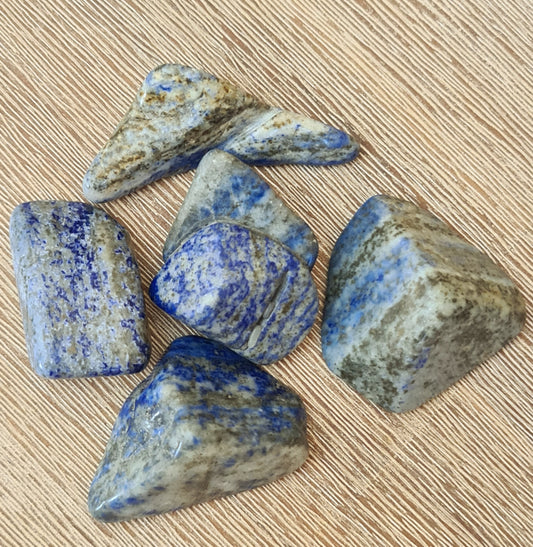 Several polished lapis lazuli chunks with a blue coloring and natural patterns, placed on a beige background.