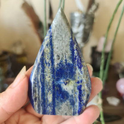 A freeform-shaped lapis lazuli stone with a marbled blue and white appearance, held in a person's hand.