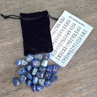 Set of blue rune stones with a black drawstring bag and rune chart on a wooden surface