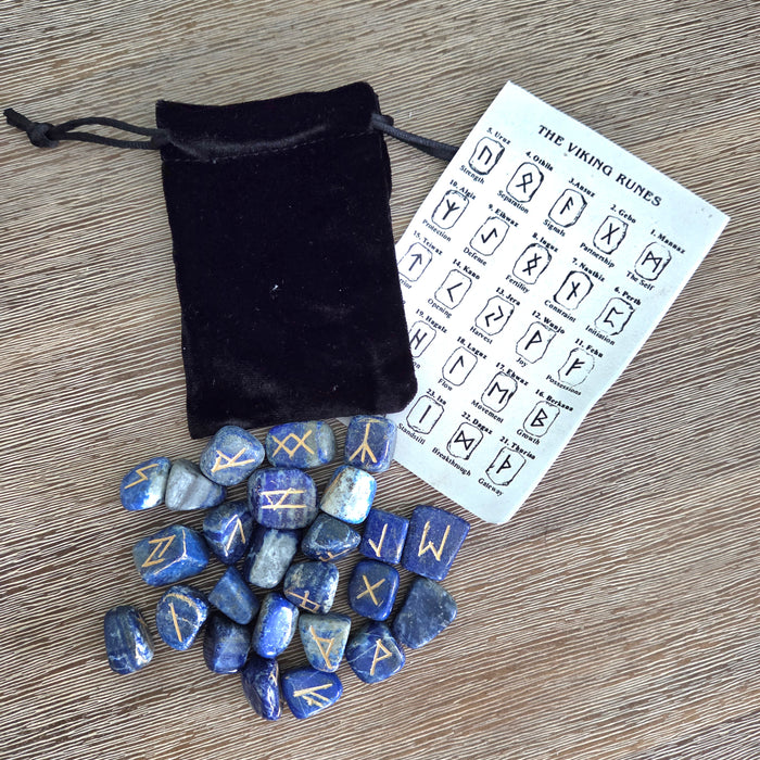 Set of blue rune stones with a black drawstring bag and rune chart on a wooden surface