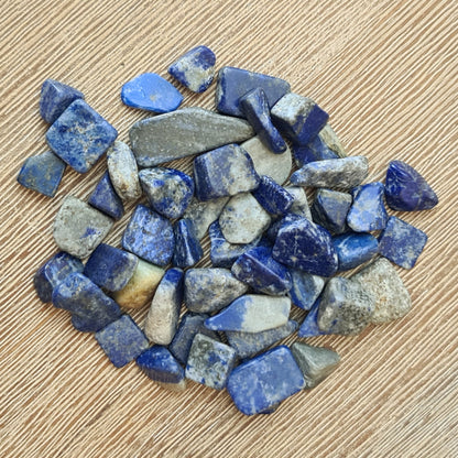 A collection of small lapis lazuli stones scattered on a wooden surface.