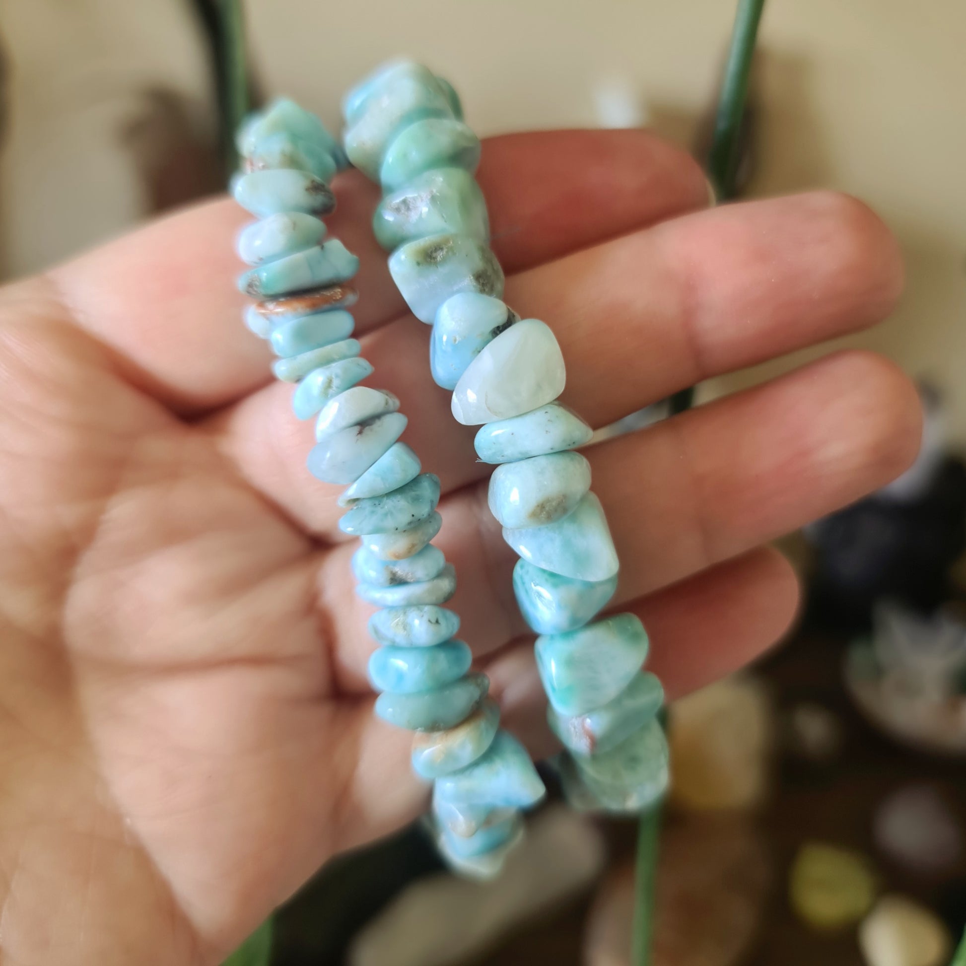 A hand holding a Larimar bracelet with blue stone beads.