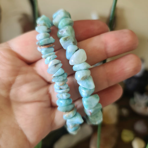 A hand holding a Larimar bracelet with blue stone beads.