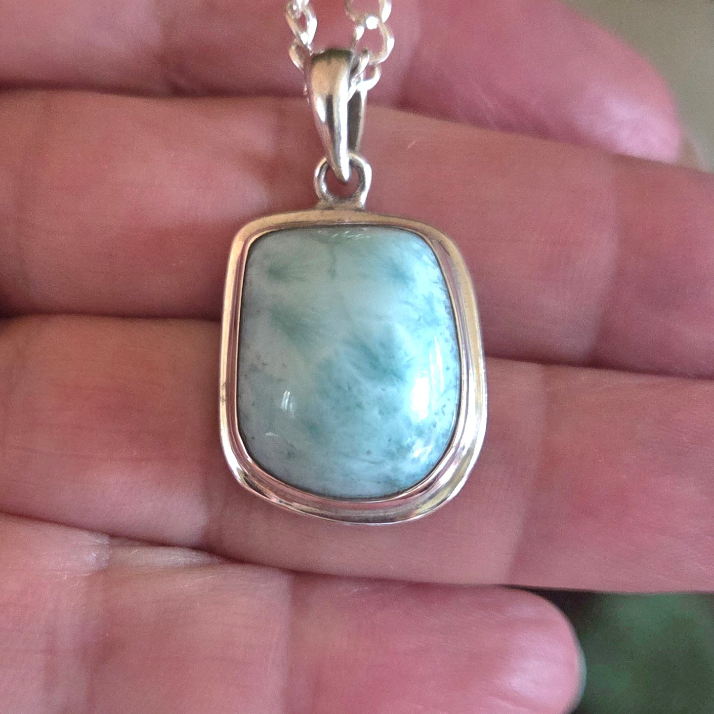 Turquoise stone pendant on a silver chain held in a hand.