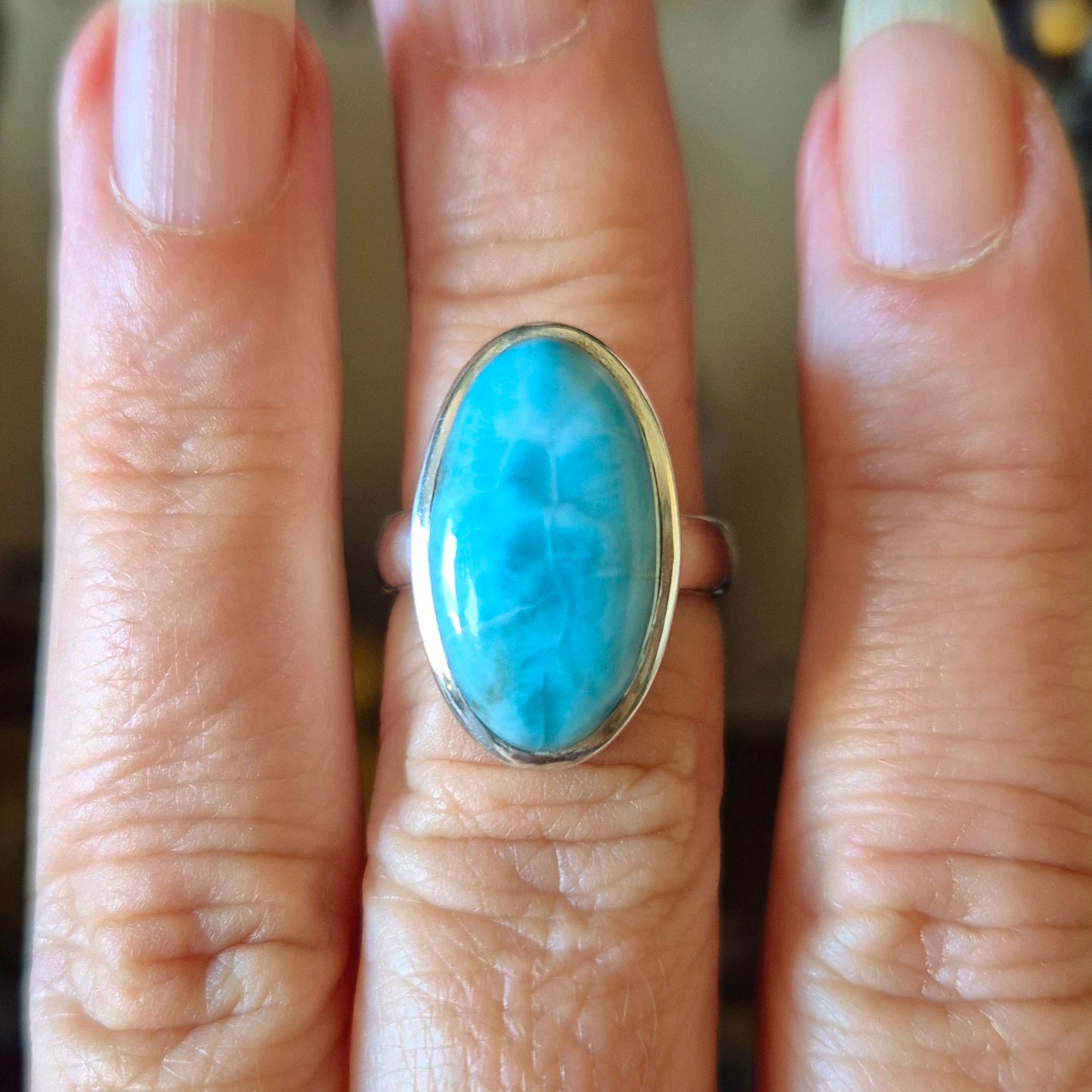 A hand wearing a blue larimar ring with a gold band.