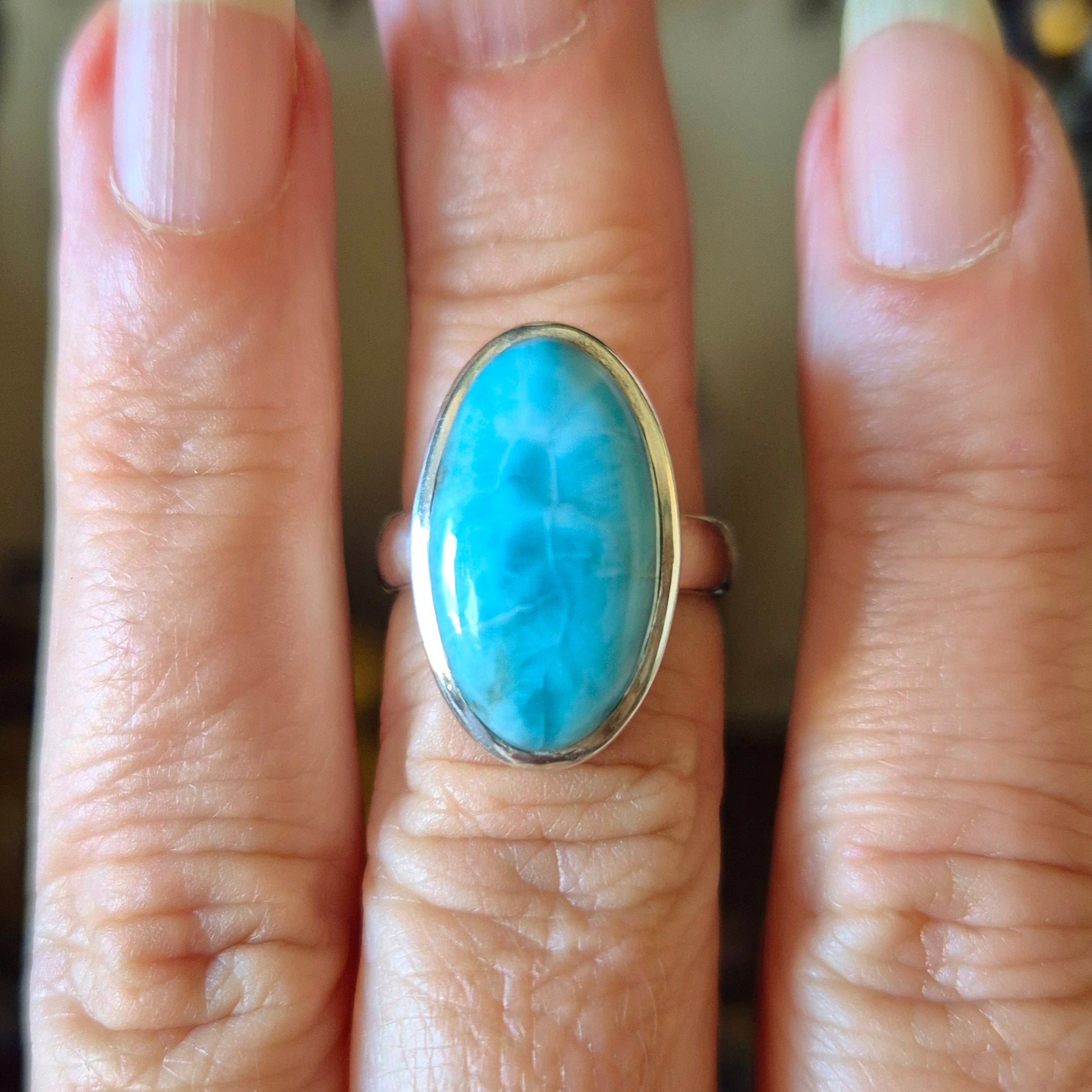 A hand wearing a blue larimar ring with a gold band.