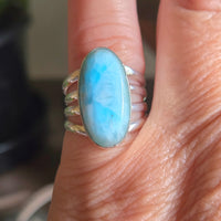 Silver ring with a large blue stone on a finger against a blurred background