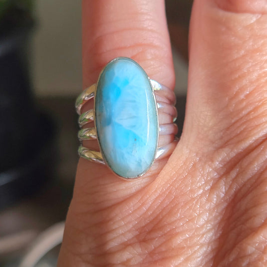 Silver ring with a large blue stone on a finger against a blurred background