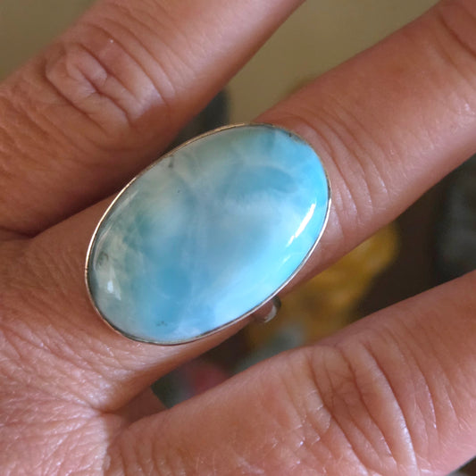 Ring with a light blue stone on a finger against a blurred background