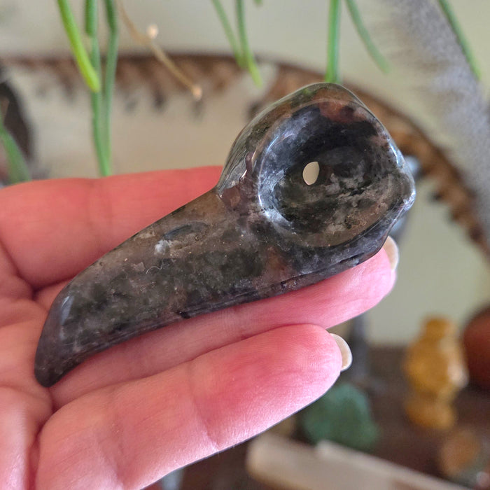 Hand holding a dark stone pipe with a blurred background