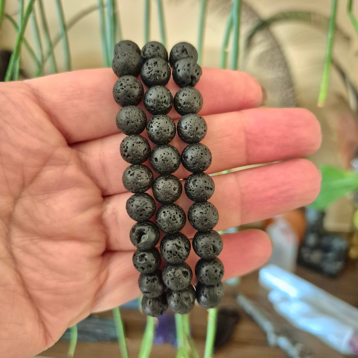 A hand holding a lava stone bracelet with black color and calcite inclusions.