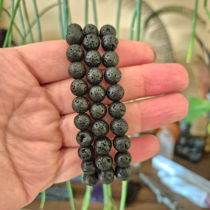 A hand holding a lava stone bracelet with black color and calcite inclusions.