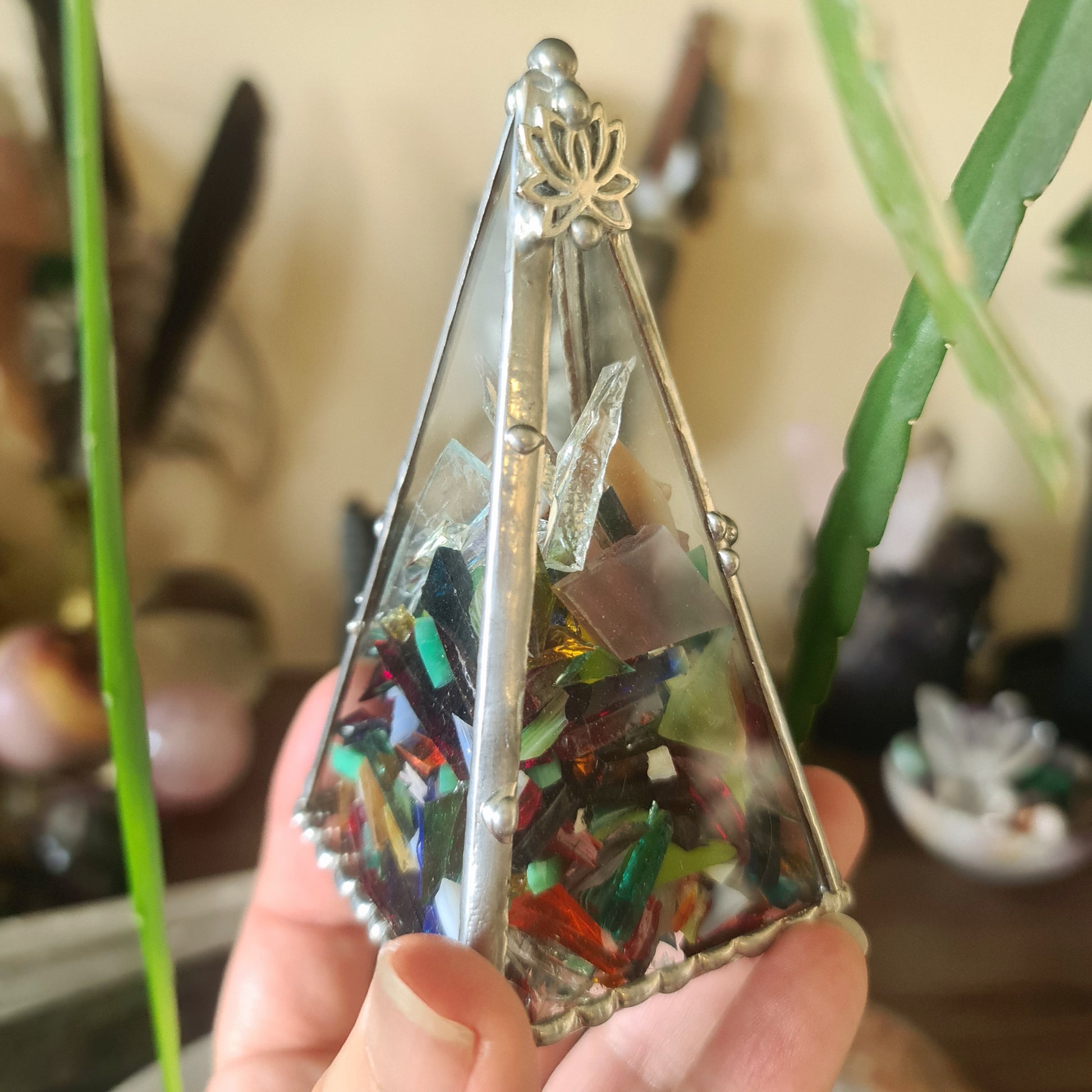 A hand holding a leadlight pyramid with multicolored glass chips and a metallic top.