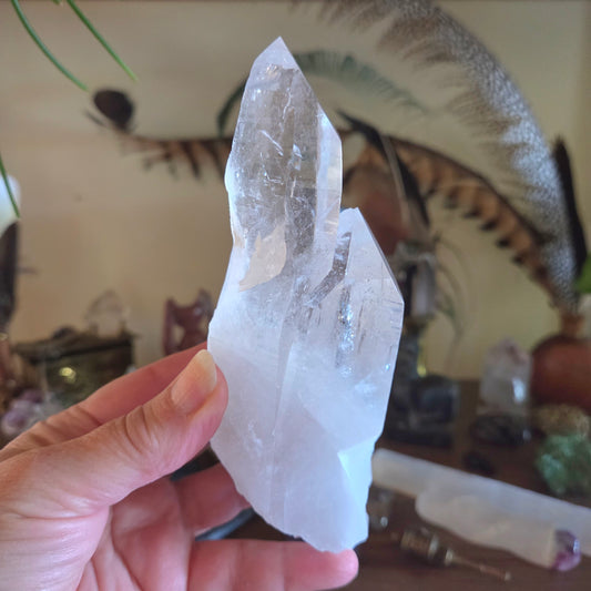 Hand holding a clear crystal with a blurred indoor setting in the background