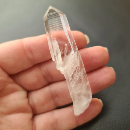 A clear, pointed Lemurian seed crystal held in a person's hand, with a blurred background.