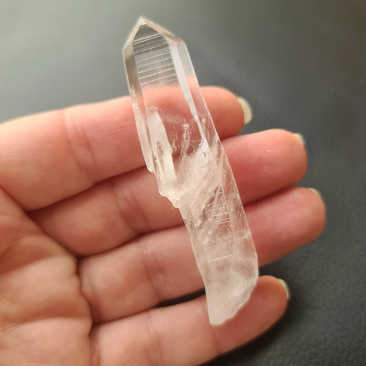 A clear, pointed Lemurian seed crystal held in a person's hand, with a blurred background.