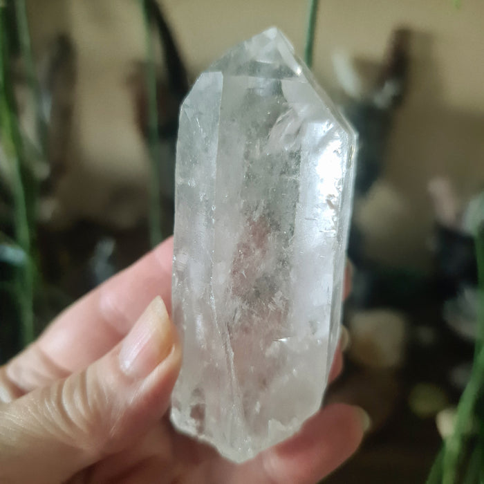 A clear, faceted Lemurian seed crystal point being held in a person's hand.