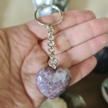A hand holding a lepidolite crystal keyring with a heart-shaped design.