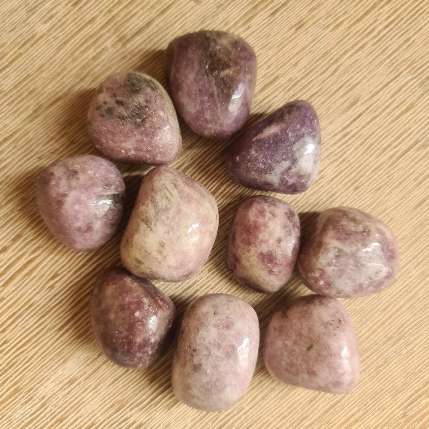 A collection of polished Lepidolite stones on a wooden surface.