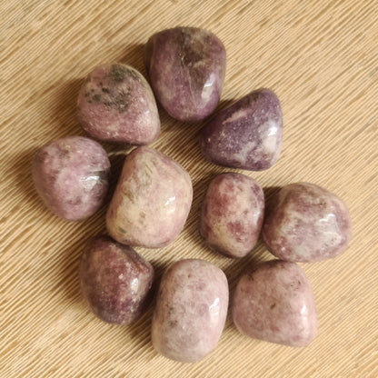 A collection of polished Lepidolite stones on a wooden surface.