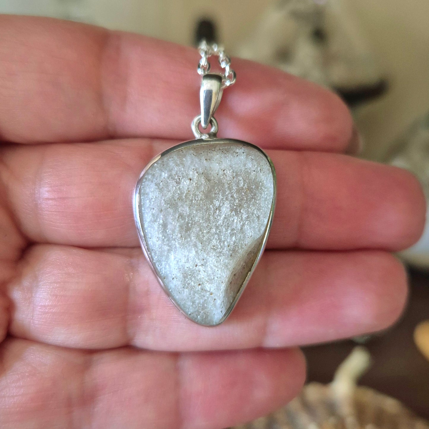 A silver-colored pendant featuring a piece of desert glass, held in a person's hand.