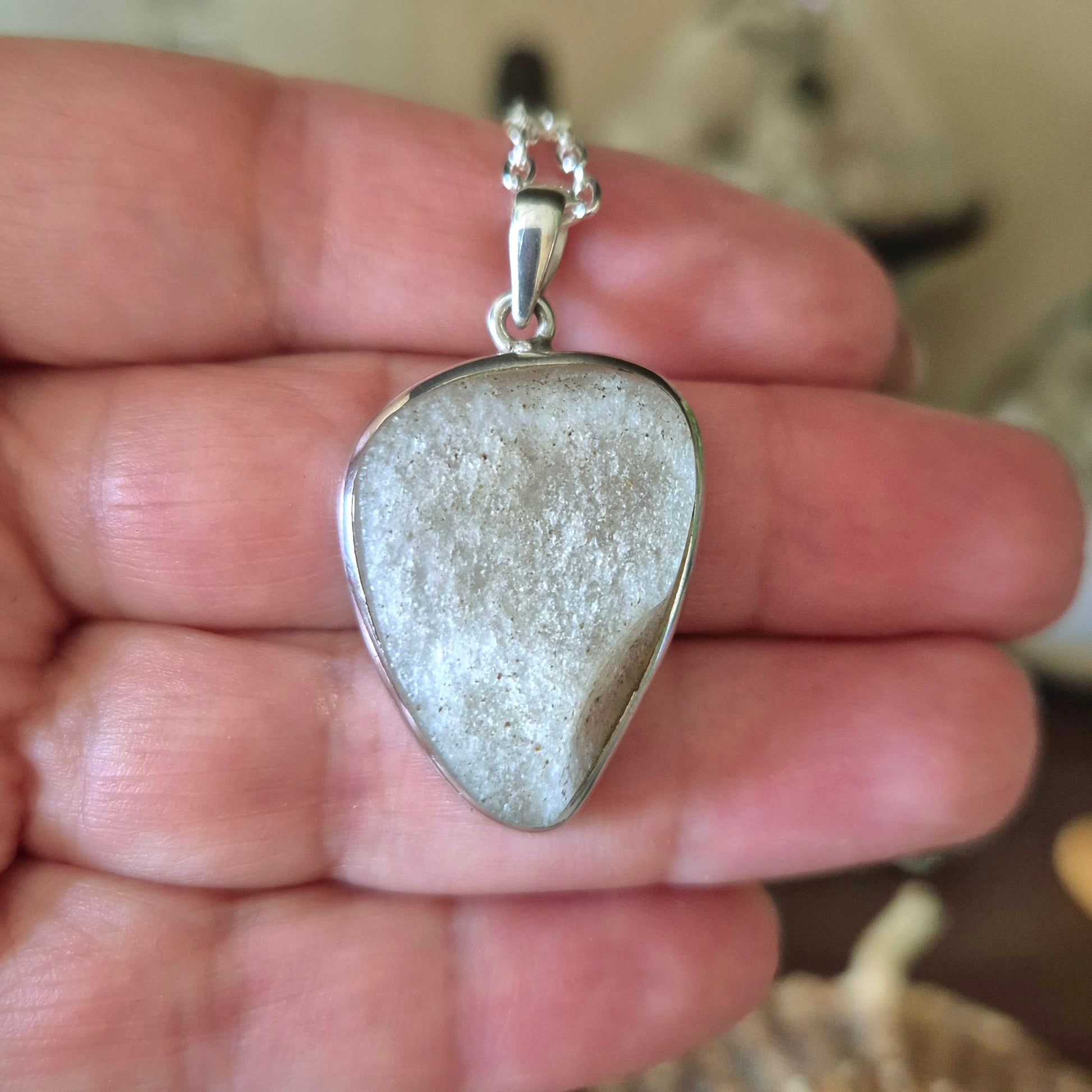 A silver-colored pendant featuring a piece of desert glass, held in a person's hand.