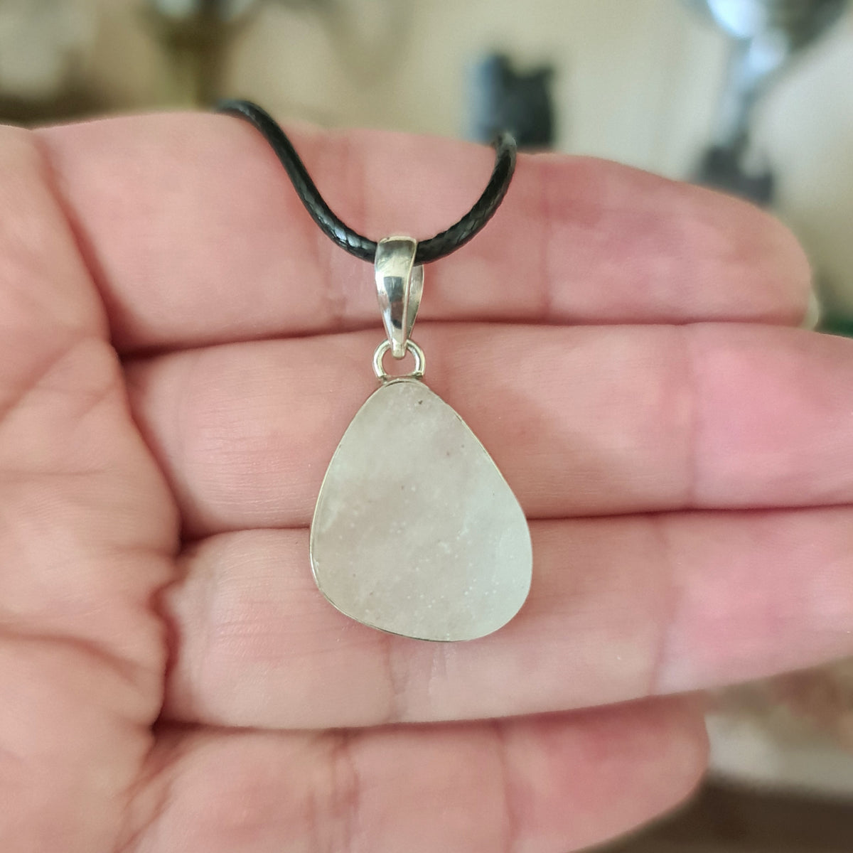 A silver pendant featuring a piece of Libyan Desert Glass, held in a hand.