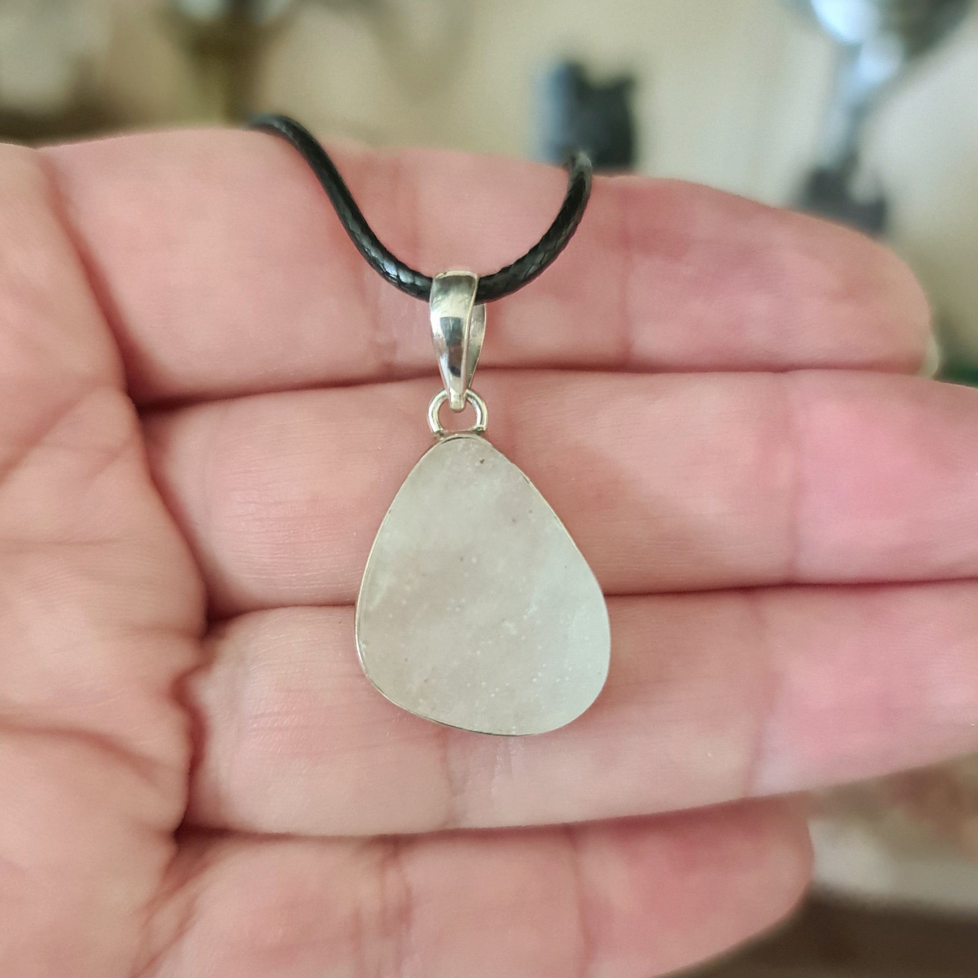 A silver pendant featuring a piece of Libyan Desert Glass, held in a hand.