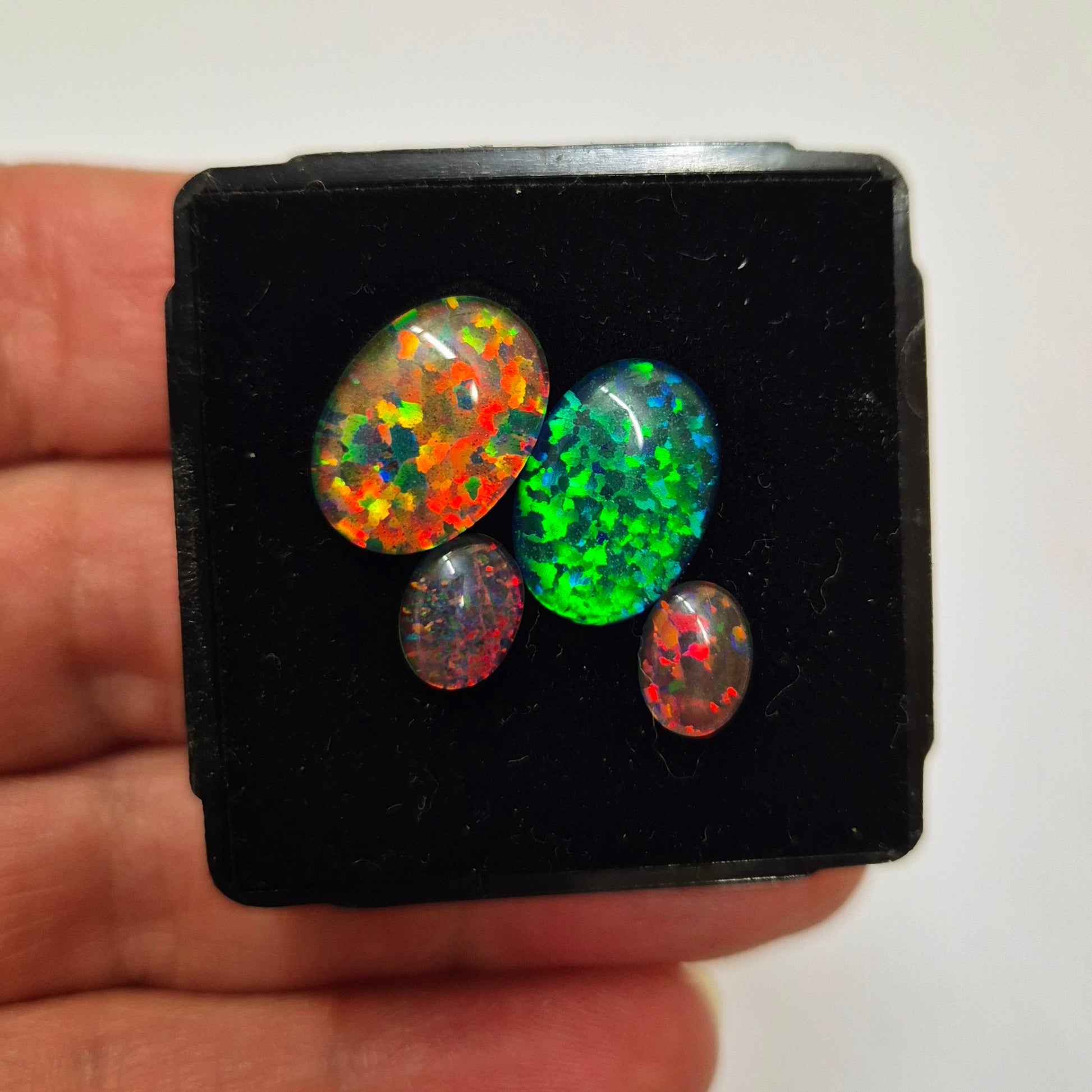 A hand holding a black box containing three opal stones with a reflective surface.