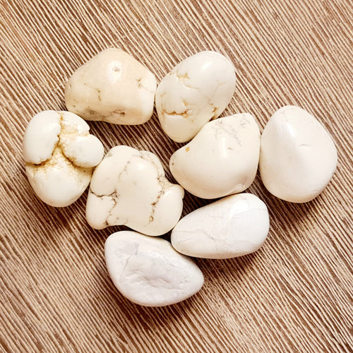 A collection of white magnesite tumble stones displayed on a textured background.