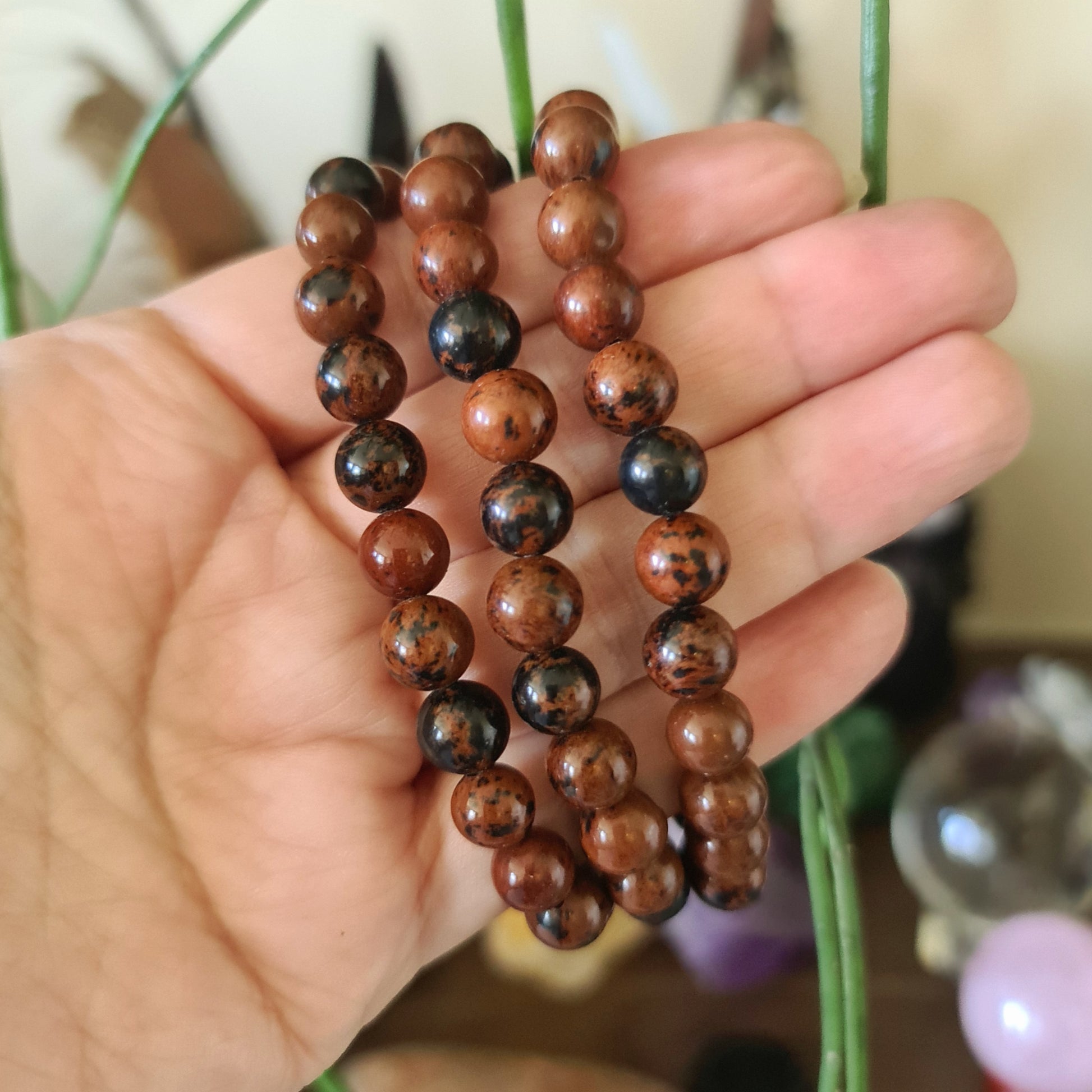 A hand holding a mahogany obsidian bead bracelet with a combination of brown and black colors.