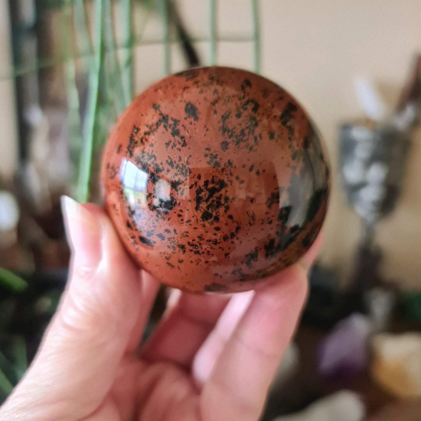 A hand holding a small spherical Mahogany Obsidian crystal with a protective and fiercely protective aura.