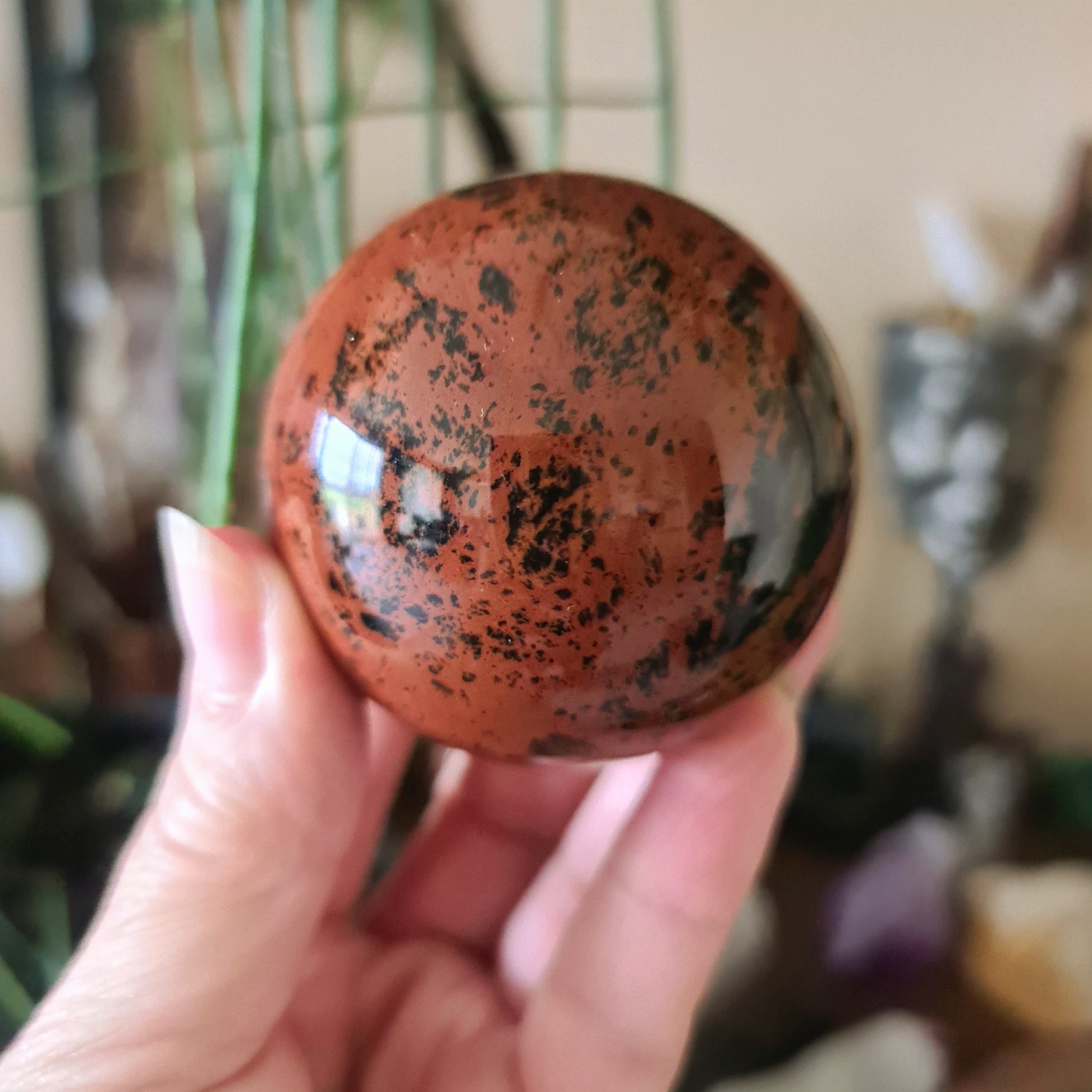 A hand holding a small spherical Mahogany Obsidian crystal with a protective and fiercely protective aura.