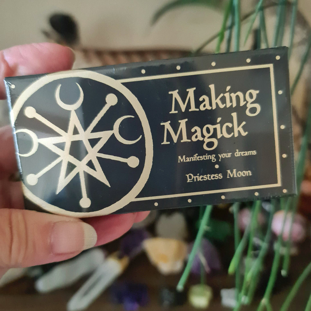 A hand holding a deck of cards with 'Making Magick' written on it, featuring mystical symbols and designs.