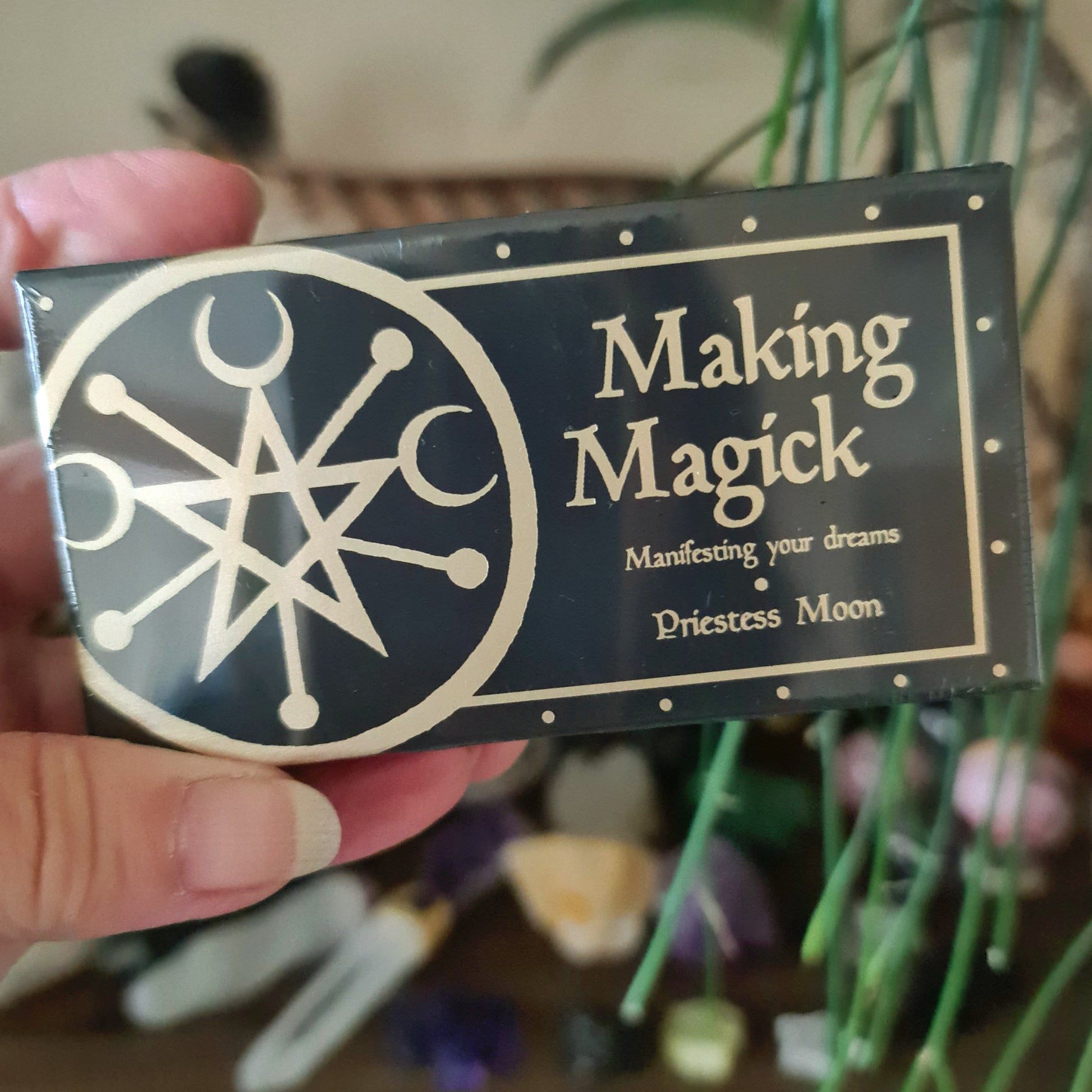 A hand holding a deck of cards with 'Making Magick' written on it, featuring mystical symbols and designs.