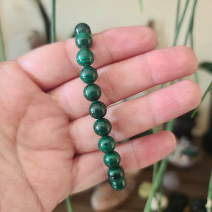 A hand holding a beaded Malachite bracelet with a green patterned design.