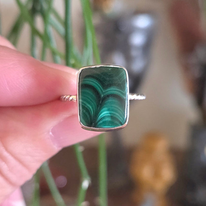 Ring with a green malachite stone held in a hand against a blurred natural background