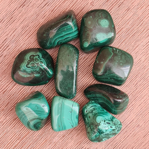 A collection of polished green malachite tumble stones displayed on a pink surface.