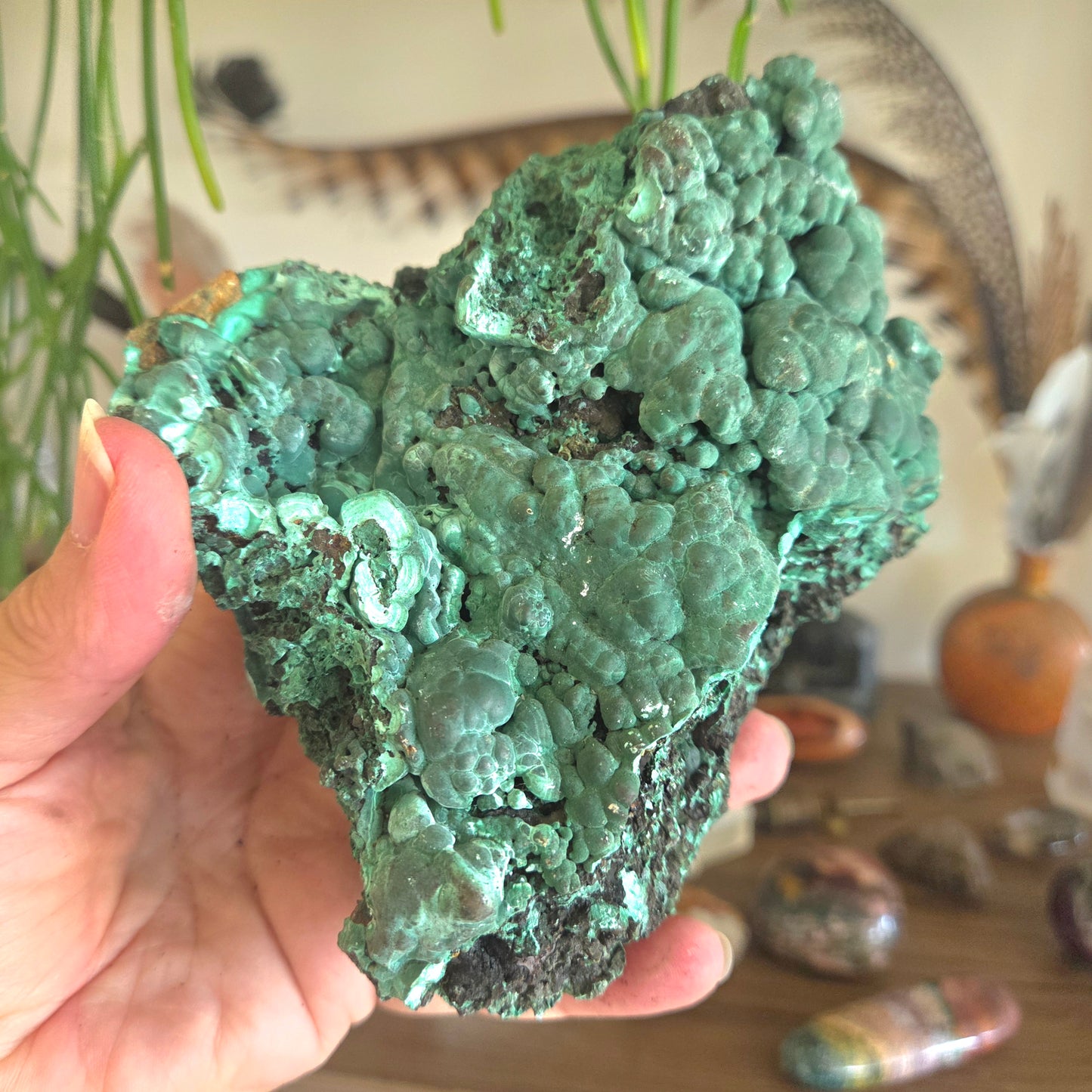 Hand holding a large green mineral specimen with a blurred indoor setting