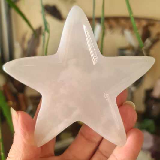 A clear, star-shaped Mangano Calcite stone held in a hand against a blurred background.