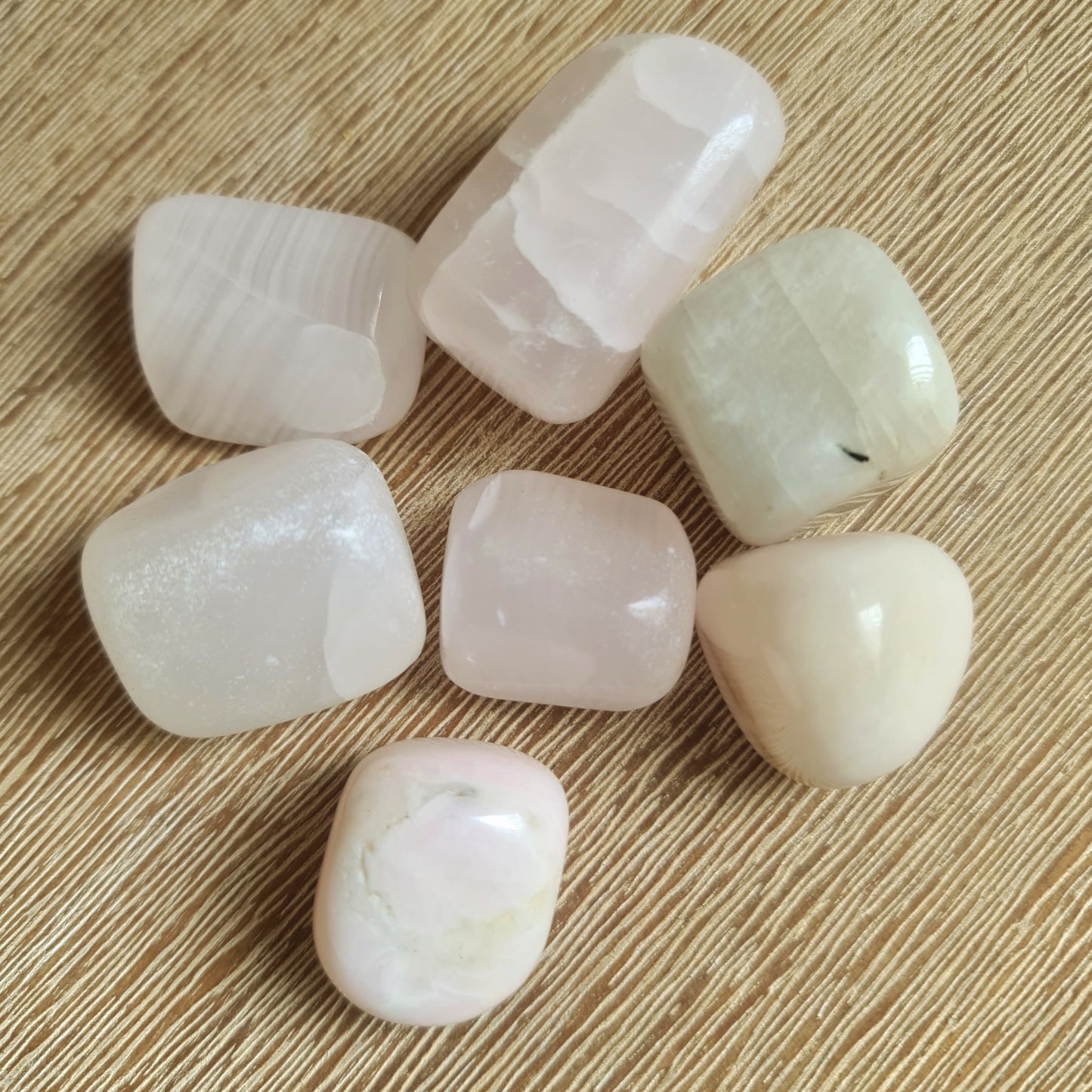 A collection of polished Mangano Calcite tumble stones with a pink and white color spectrum.