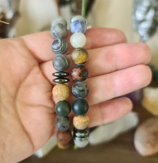 A hand holding a men's chakra bracelet with various multicolored gemstone beads.