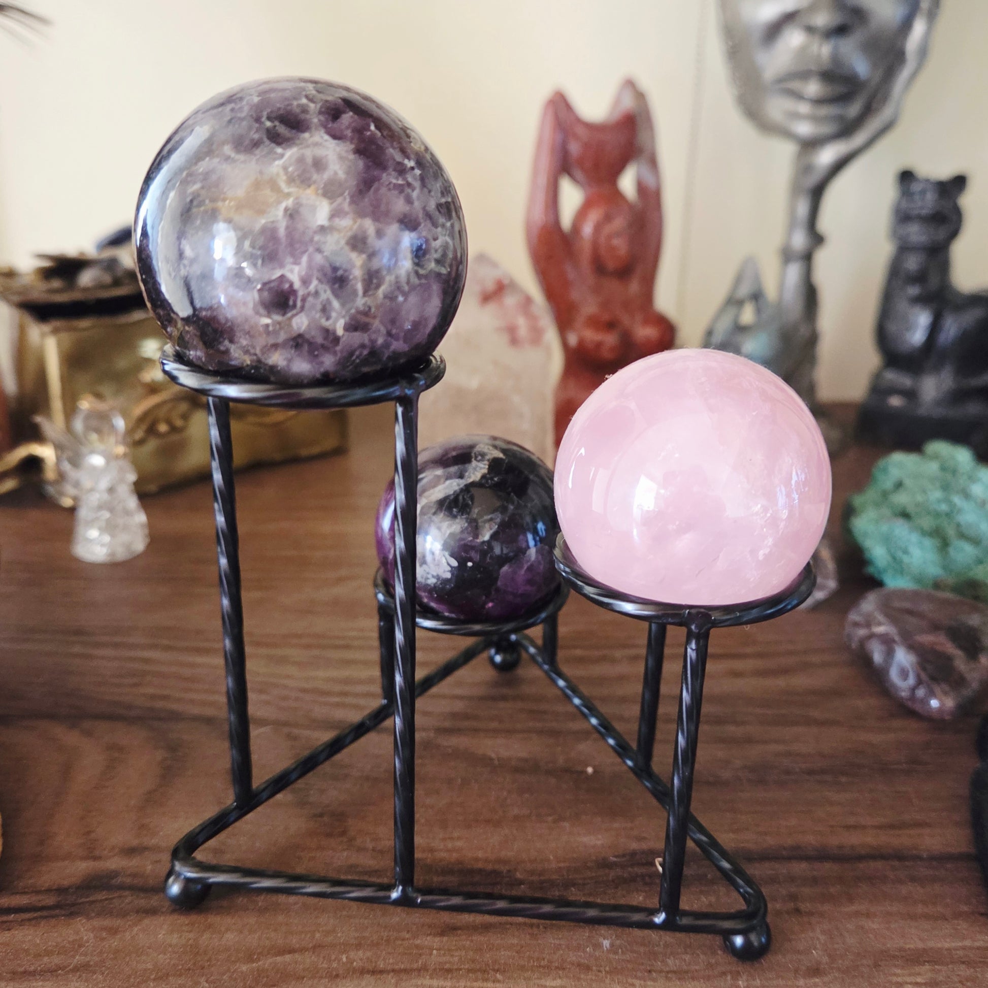 A metal stand holding three spherical objects, with each sphere having a different color and pattern. The stand is placed on a wooden surface and there are various items in the background.